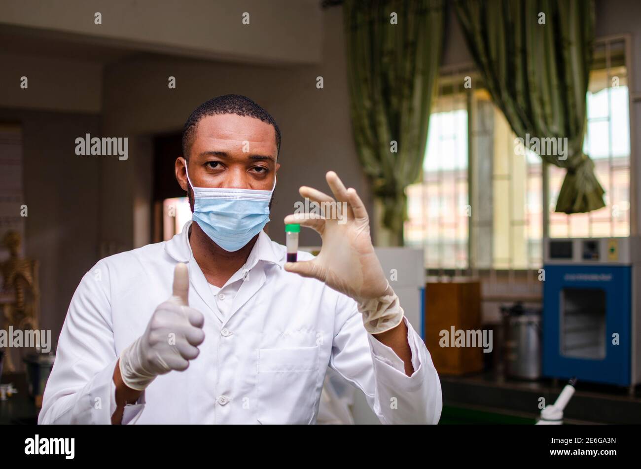 Giovane scienziato di laboratorio nero che indossa una maschera al naso, osservando un campione di sangue in mano Foto Stock