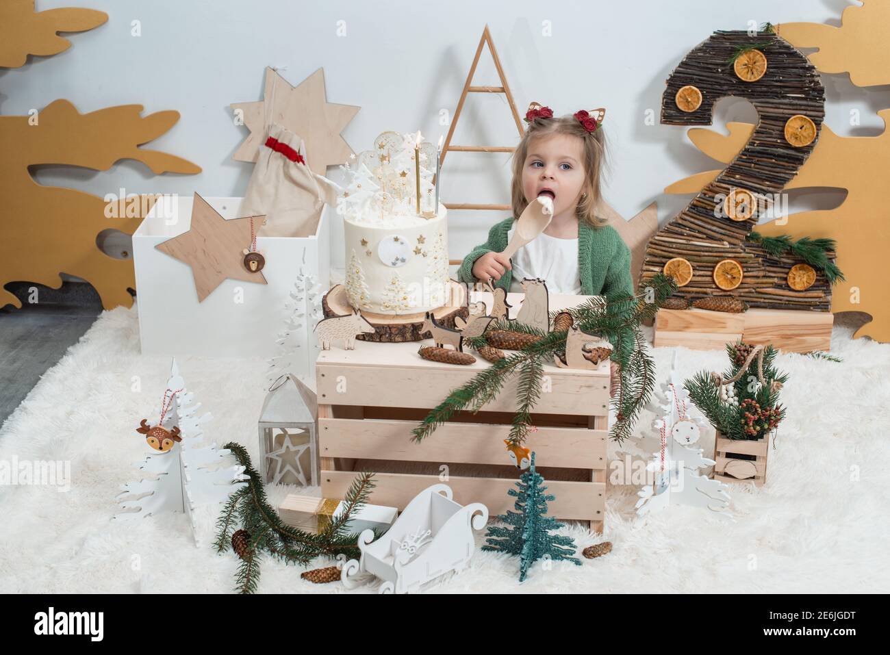 Decorazioni per compleanno invernali per bambini. 2 anni. Carino bambina in  un cardigan verde vicino torta di compleanno bianca Foto stock - Alamy