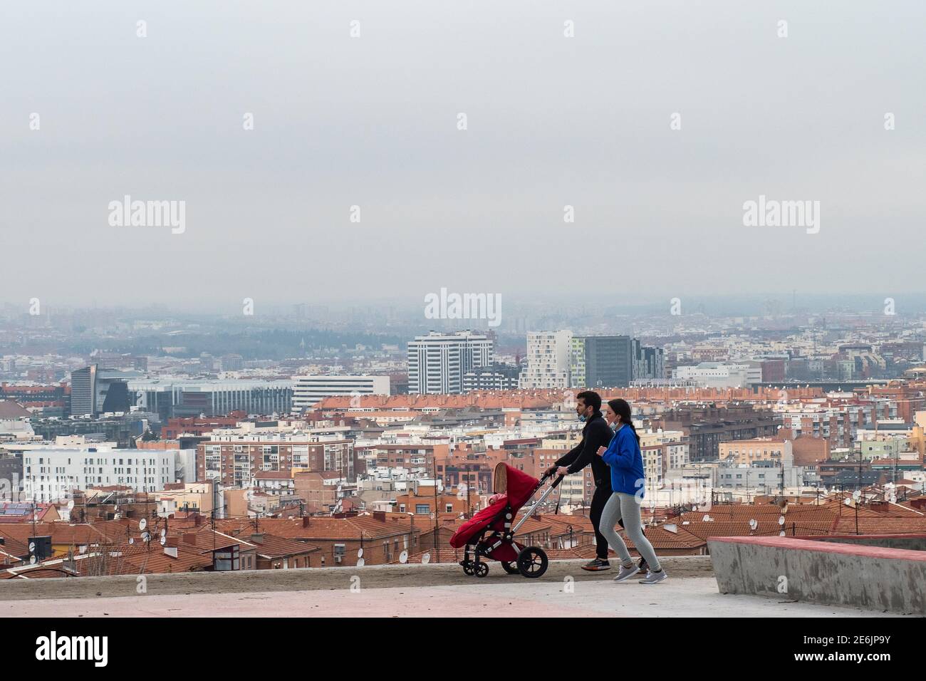 Madrid, Spagna. 29 gennaio 2021. Una coppia si esercita indossando le maschere del viso nel collo, mentre spingendo il passeggino del loro bambino con la vista dei tetti di Madrid. Il Vice Ministro della Sanità pubblica e del piano Covid-19, Antonio Zapatero, ha sottolineato oggi che 'a Madrid vi è una situazione di alta trasmissione comunitaria, sebbene tutto indica un rallentamento e un cambiamento di tendenza, che diminuirà i casi con coronavirus nella regione, Tuttavia la pressione sanitaria continua ad essere molto alta, con 4,956 pazienti, 700 dei quali sono in UTI 'Credit: Marcos del Mazo/Alamy Live News Foto Stock