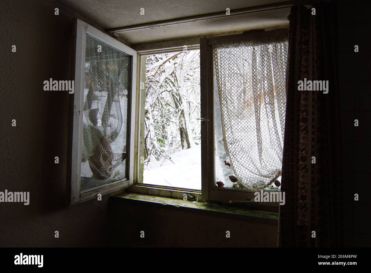 finestra aperta con tende antiche in una casa abbandonata, fuori c'è neve Foto Stock