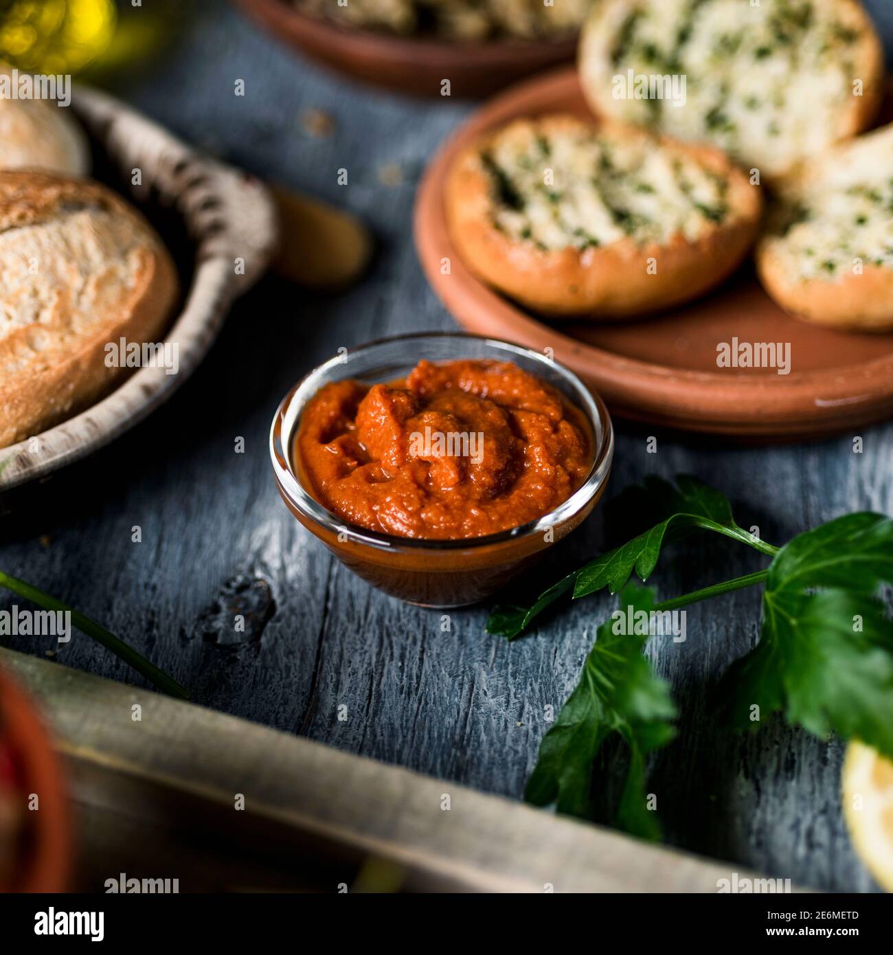 una ciotola di vetro con una versione vegana della tipica sobrasada spagnola, fatta con patata dolce rossa, su un tavolo in legno rustico grigio accanto ad alcune diverse k. Foto Stock