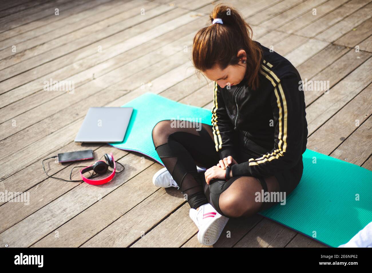 Giovane donna in forma che controlla l'orologio intelligente mentre si siede sullo yoga mat Foto Stock