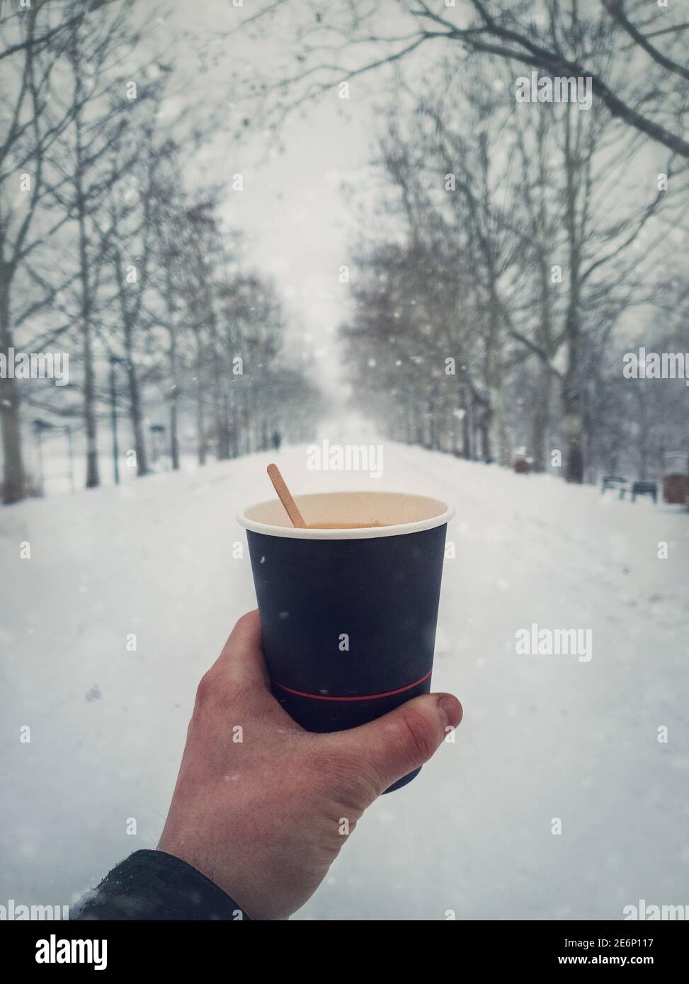 La persona tiene una tazza di caffè caldo fresco all'aperto nel parco invernale in una fredda mattina innevata. Primo piano ripresa verticale. Carta riciclabile Foto Stock