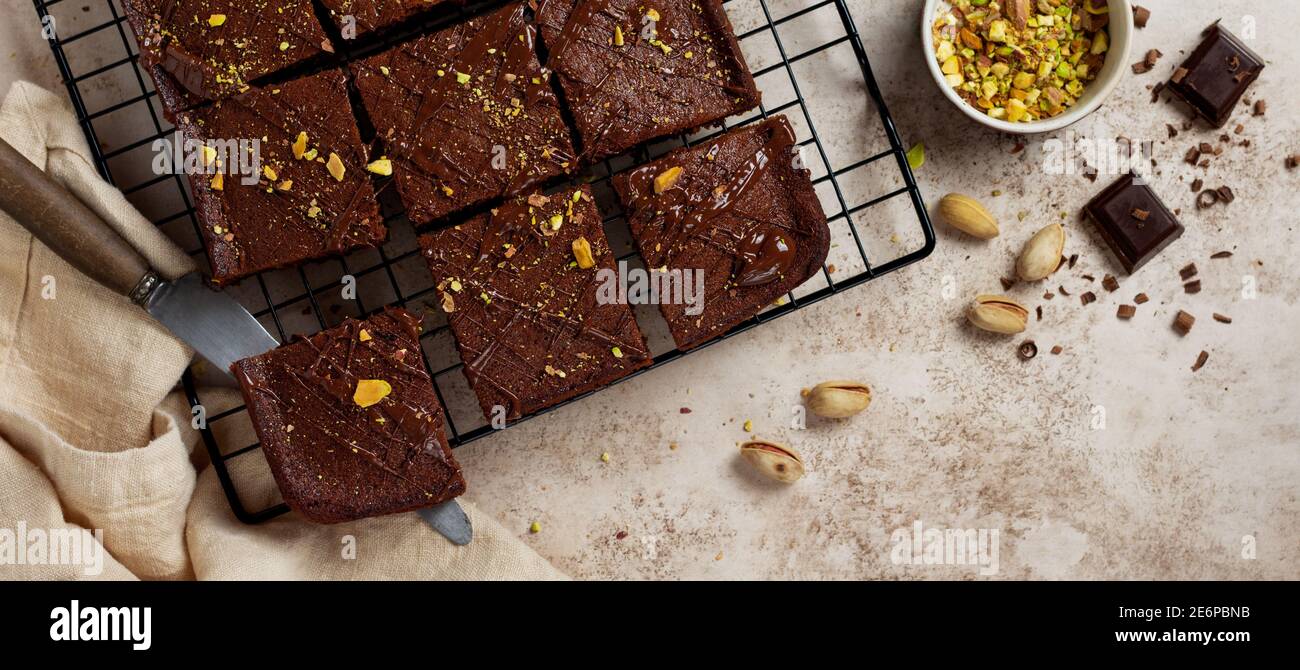 Quadrati di cioccolato con pistacchio e fragole su un supporto metallico su uno sfondo di pietra chiaro, vista dall'alto, composizione orizzontale. Disposizione piatta. Foto Stock