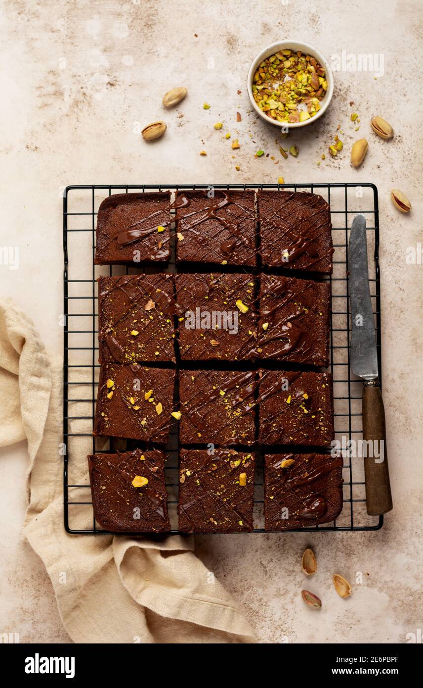 Quadrati di cioccolato con pistacchio e fragole su un supporto metallico su uno sfondo di pietra chiaro, vista dall'alto, composizione orizzontale. Disposizione piatta. Foto Stock
