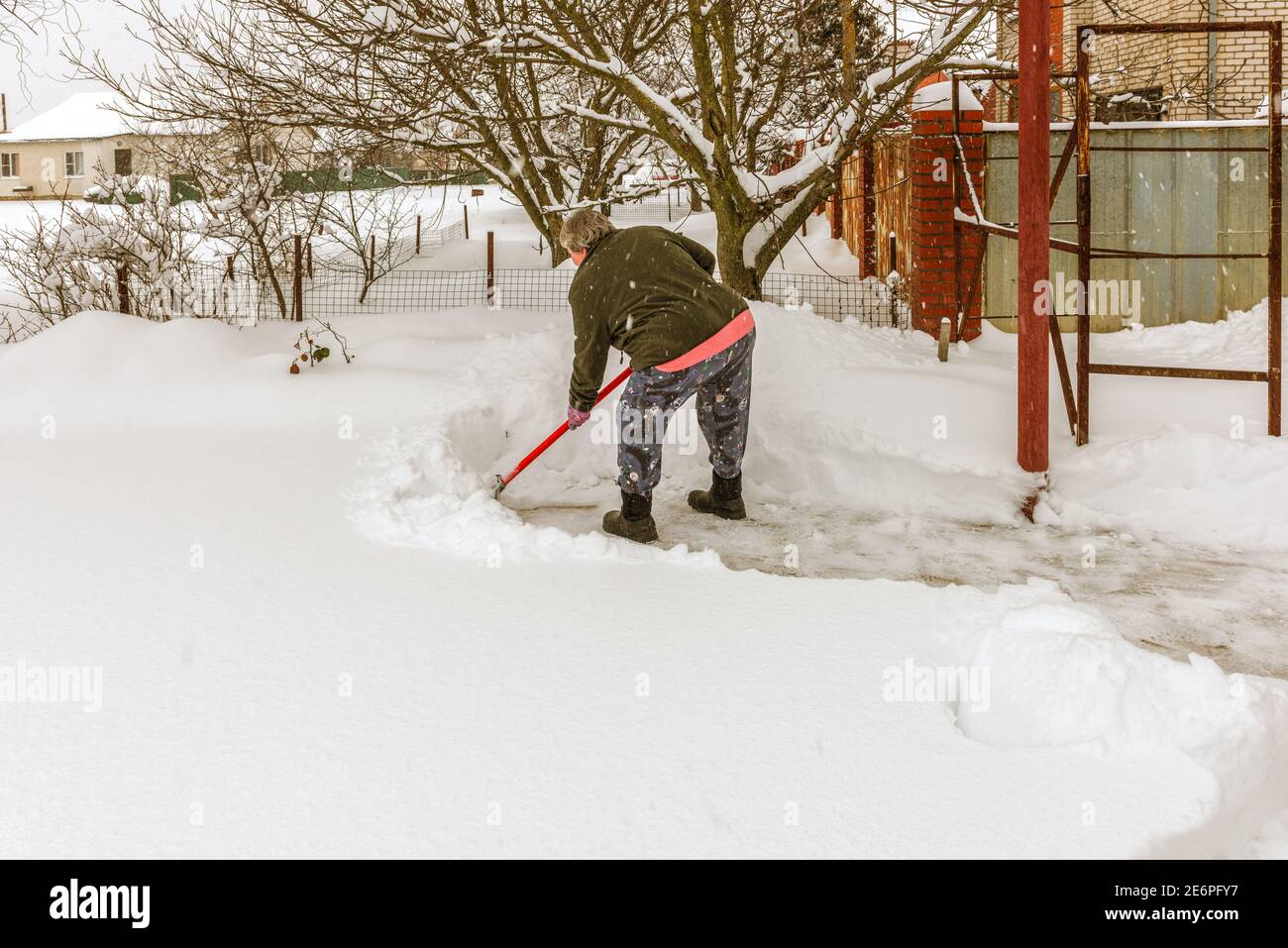 Una donna anziana rimuove la neve dalla strada che la sta vicino casa Foto Stock