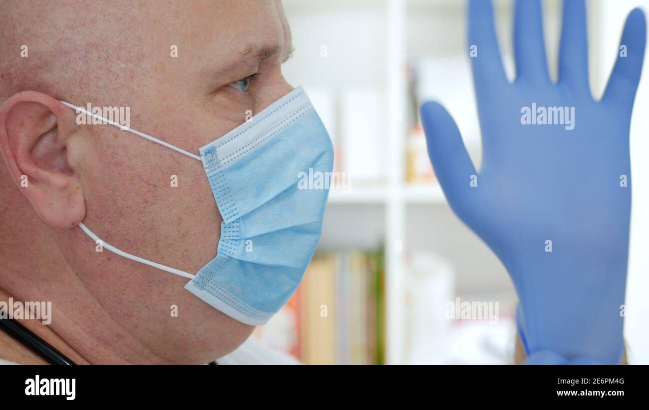Il medico indossando la maschera protettiva del viso, mette i guanti chirurgici sulle sue mani. Foto Stock