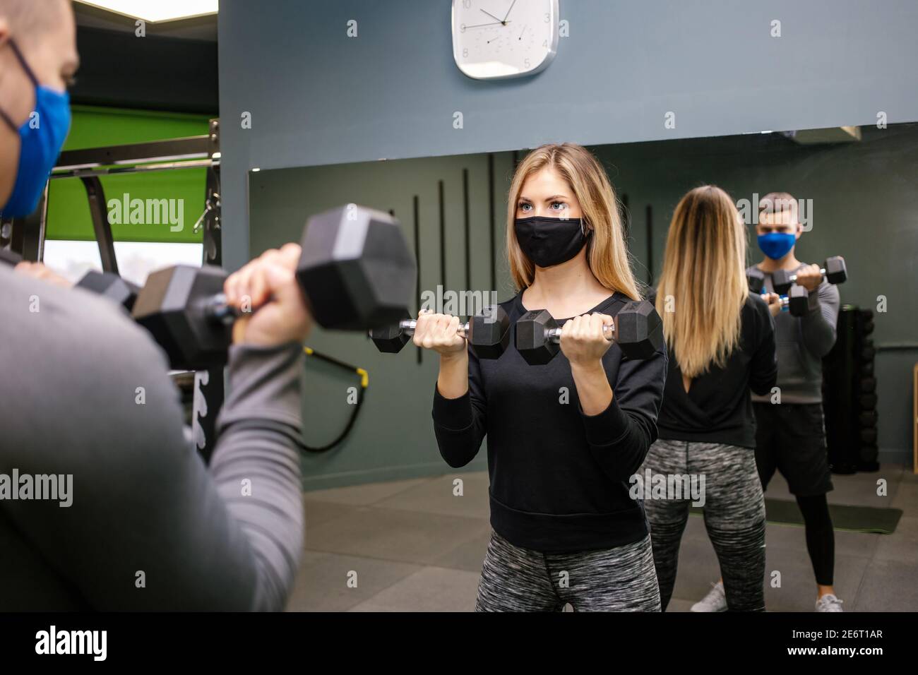 Giovane bella donna con maschera protettiva che lavora con personal trainer in palestra durante la pandemia di Covid-19. Persona sportiva in maschera protettiva. Foto Stock