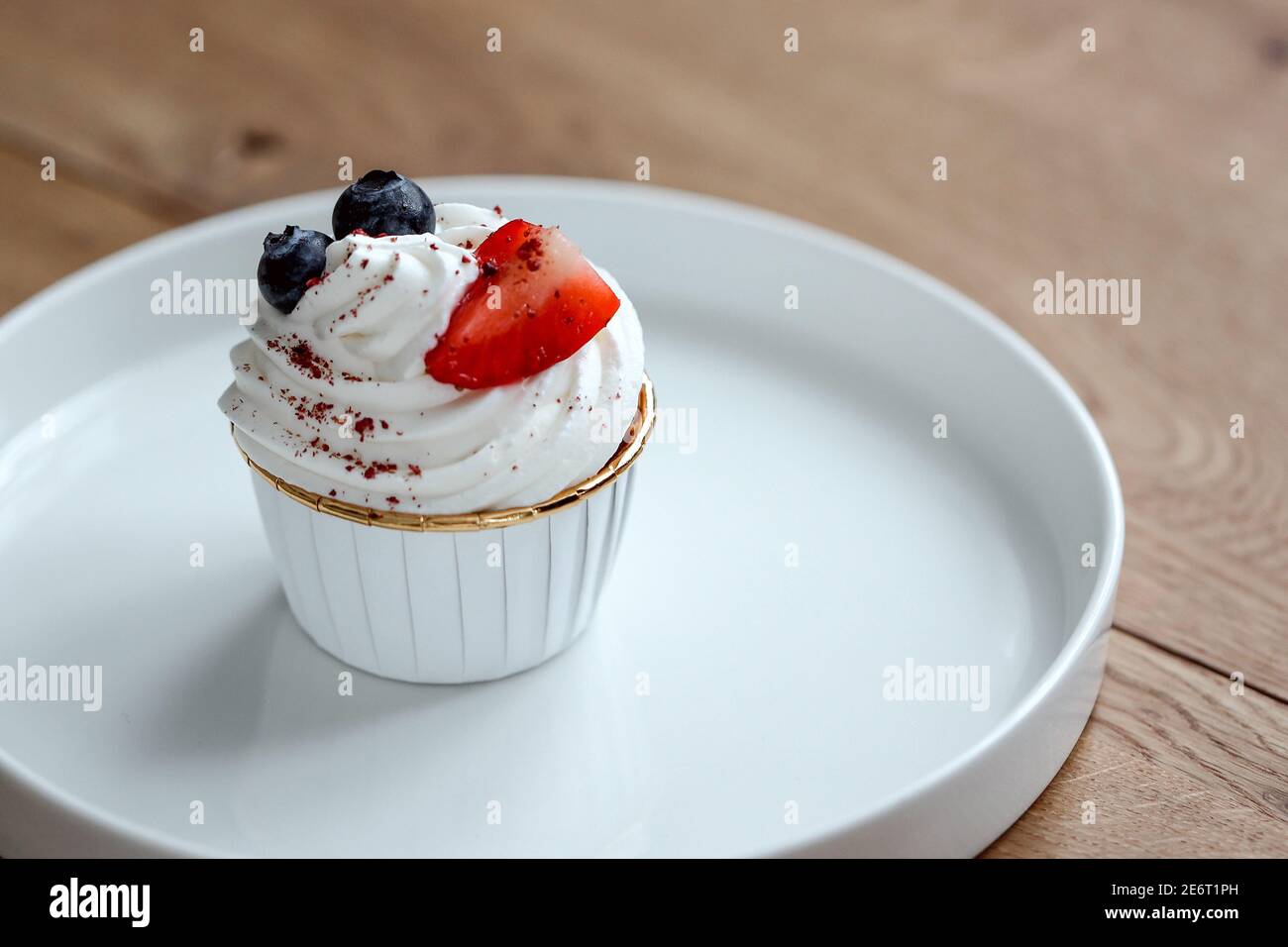 Delizioso cupcake con panna montata, fragola fresca, mirtillo su piatto bianco. Foto Stock