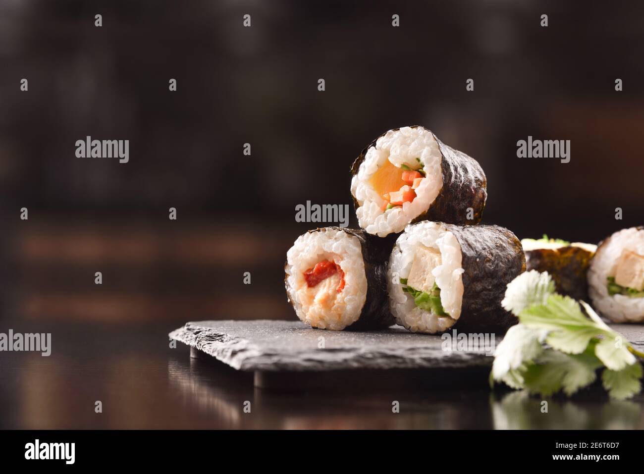 Dettaglio di sushi maki assortiti su piastra d'ardesia e bastoni su tavolo di legno nero. Vista frontale. Composizione orizzontale. Foto Stock