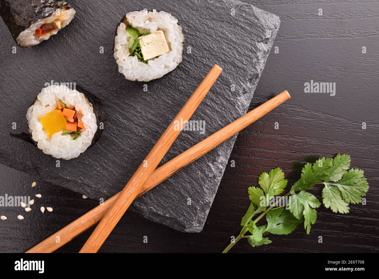 Dettaglio di sushi maki assortiti su piastra d'ardesia e bastoni su tavolo di legno nero. Vista dall'alto. Composizione orizzontale. Foto Stock