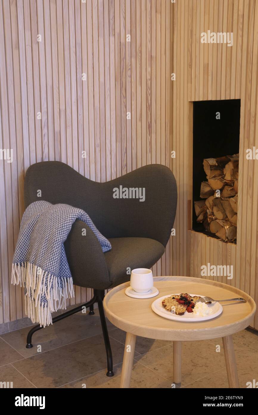 Svezia, Lapponia, Norrbotten County, Harads, waffle e tè messi su un tavolo vicino a una stufa a legna di design nella sala del bagno artico hotel con la sua raffinata decorazione scandinava Foto Stock
