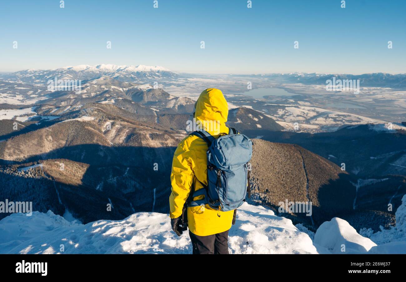 Concept composito di avventura, esplorazione e stile di vita. Uomo avventuroso vestito giacca giallo softshell brillante che utilizza durante la vetta innevata di montagna. Foto Stock