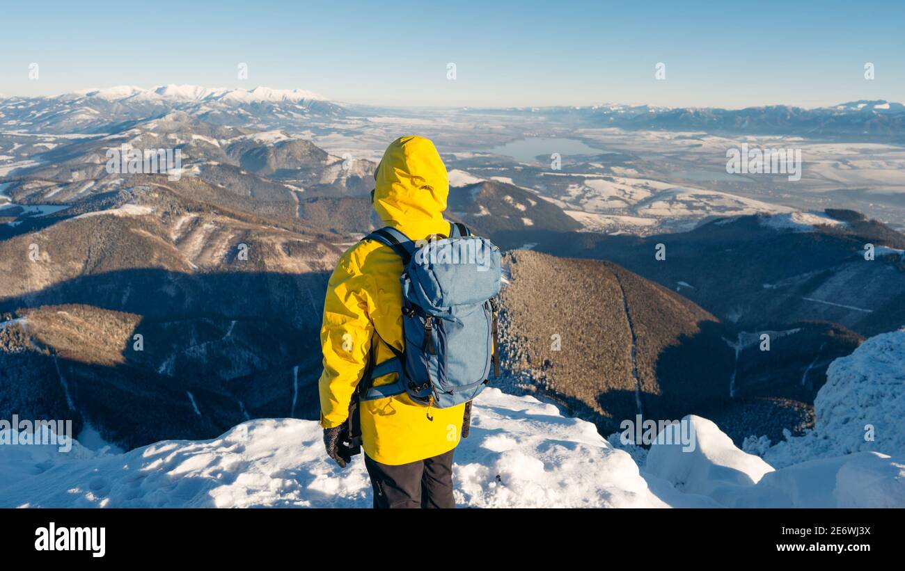 Concept composito di avventura, esplorazione e stile di vita. Uomo avventuroso vestito giacca giallo softshell brillante che utilizza durante la vetta innevata di montagna. Foto Stock