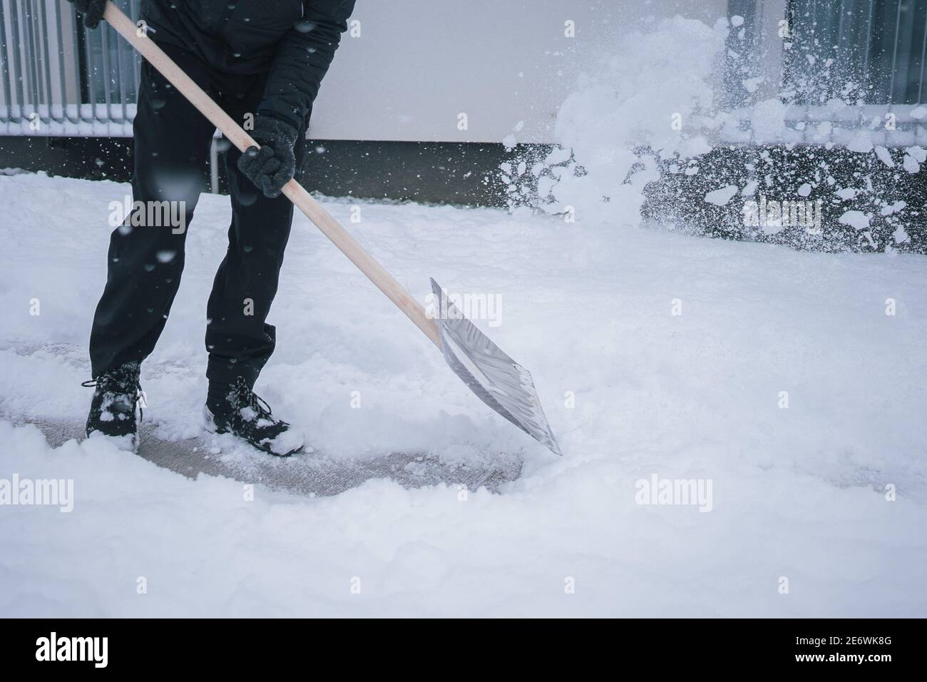 L'uomo sta liberando l'area di parcheggio accanto alla casa. Bell'uomo con maschera facciale che tiene la pala e che tovola neve bianca fresca. Stagione invernale Covid. Foto Stock