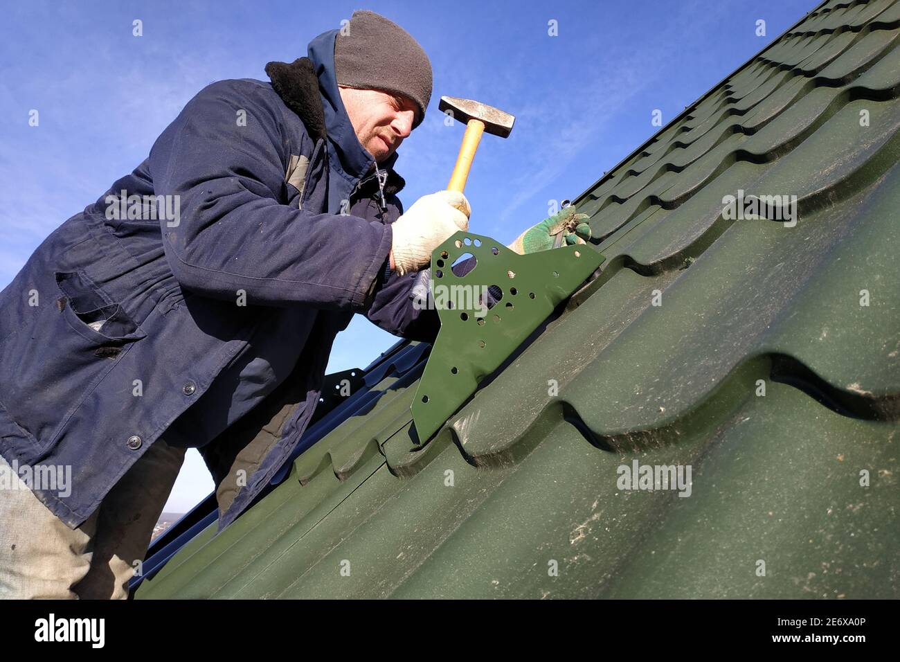 Il padrone lavora sul tetto di una casa privata senza assicurazione, il lavoro è eseguito nella stagione fredda, il lavoratore si comporta con attenzione, il tetto è Foto Stock