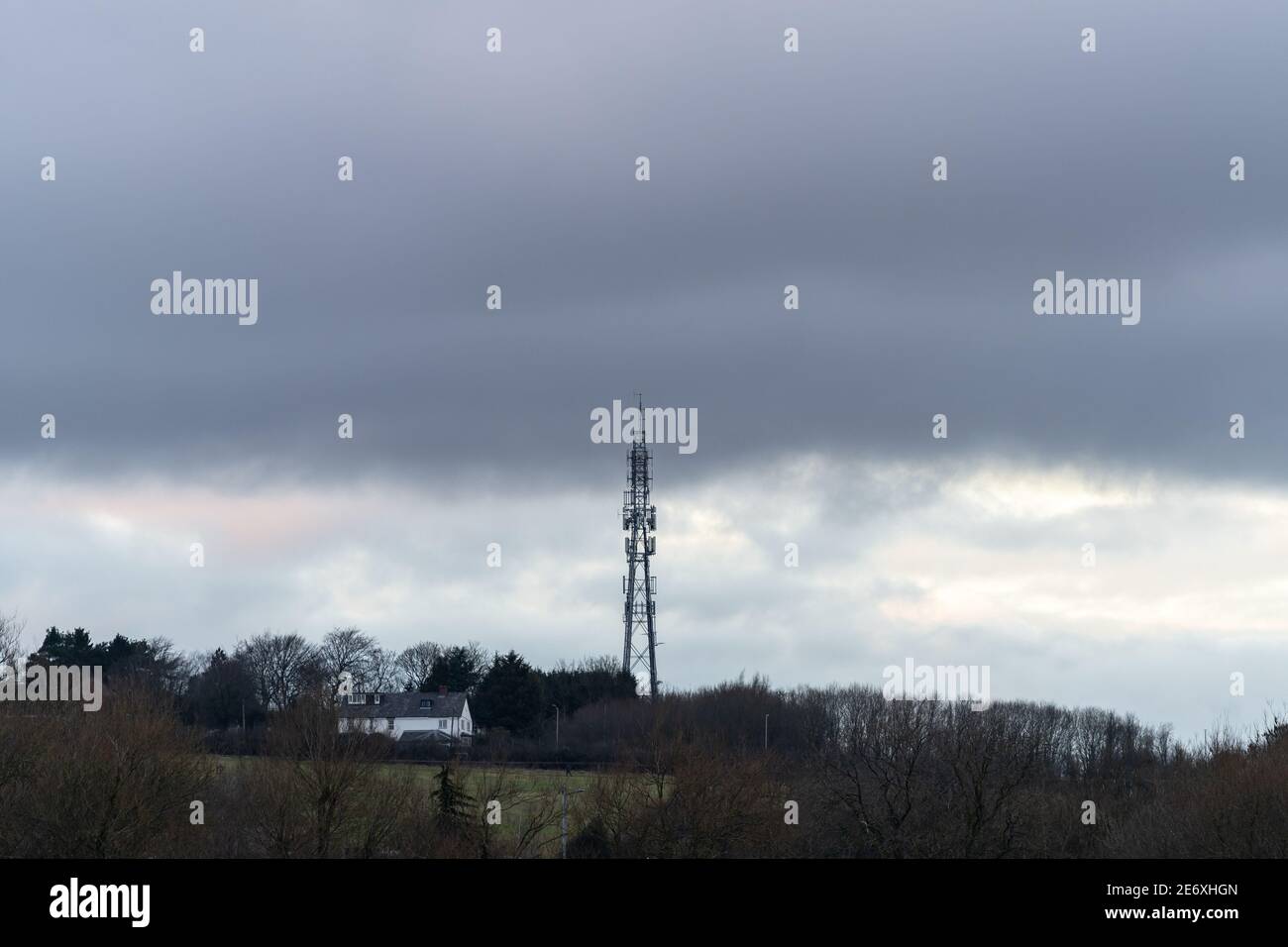 Grande rete mobile 5g telefono satellite trasmettitore torre montante avanti a case sulla collina moody cielo nuvoloso grigio scuro nuvoloso causa silhouette Foto Stock
