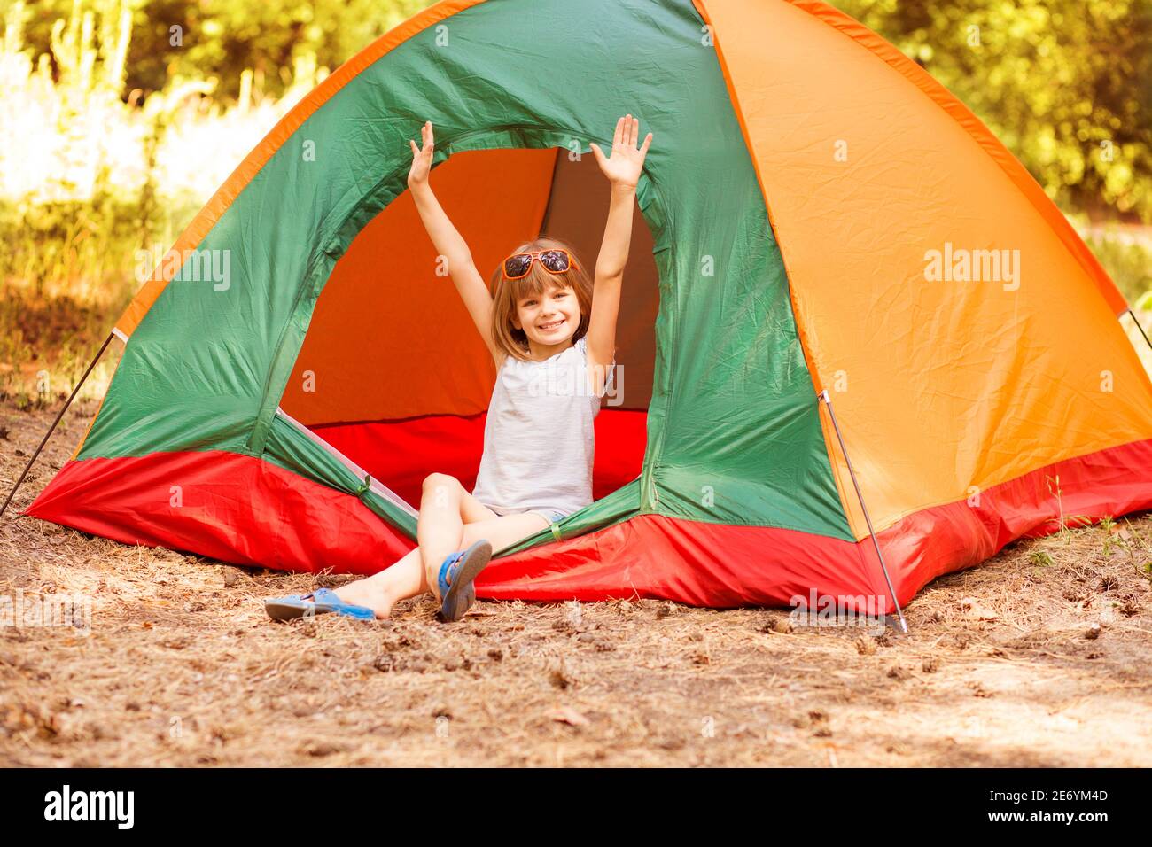 felice bambina in tenda da campeggio godetevi le vacanze nella foresta con le mani in su. Foto Stock
