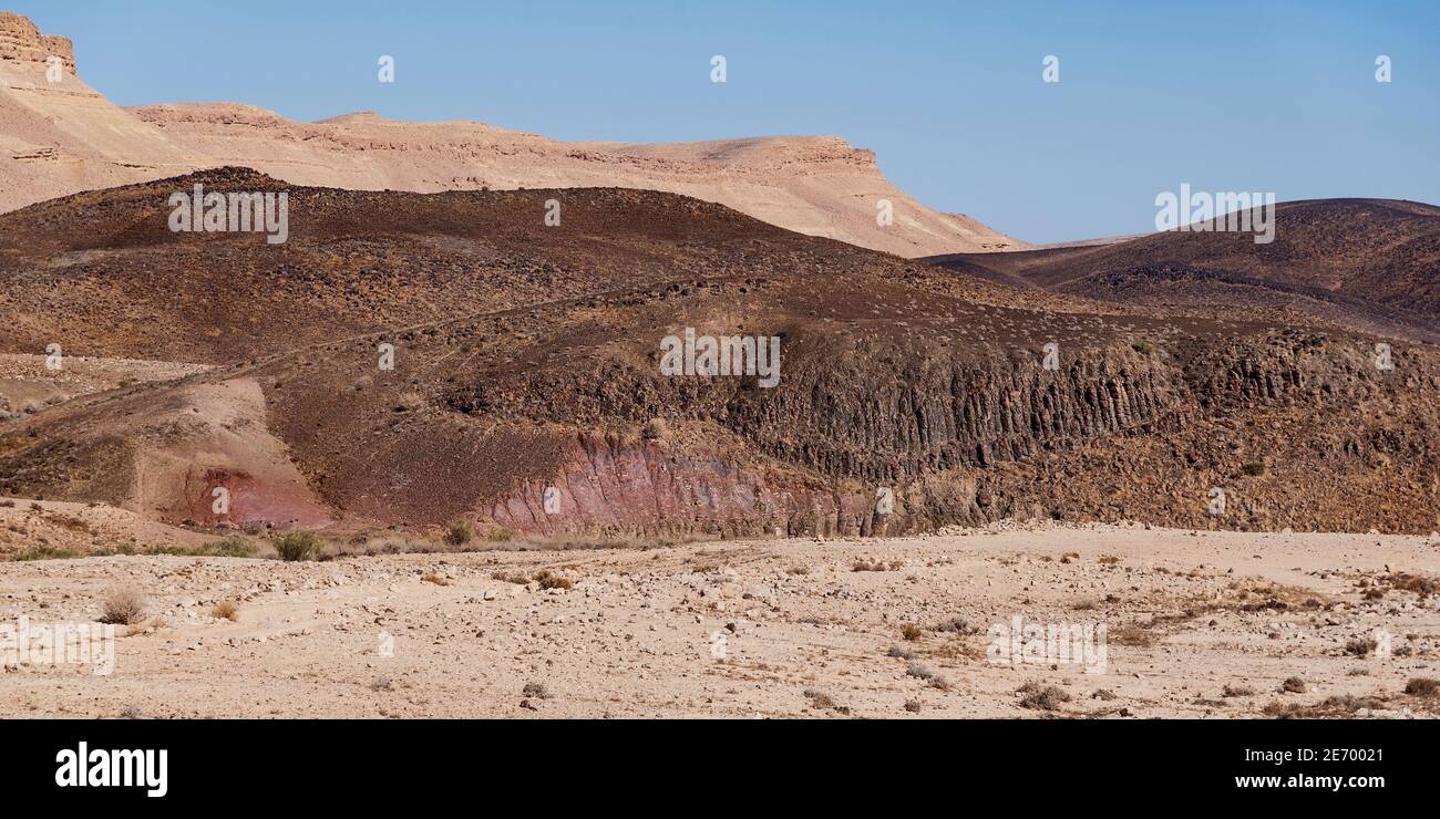 basalto collina con prismi nel processo di disgregamento in terra di argilla rossa e rosa con il bordo nord del cratere maktesh ramon in israele Foto Stock