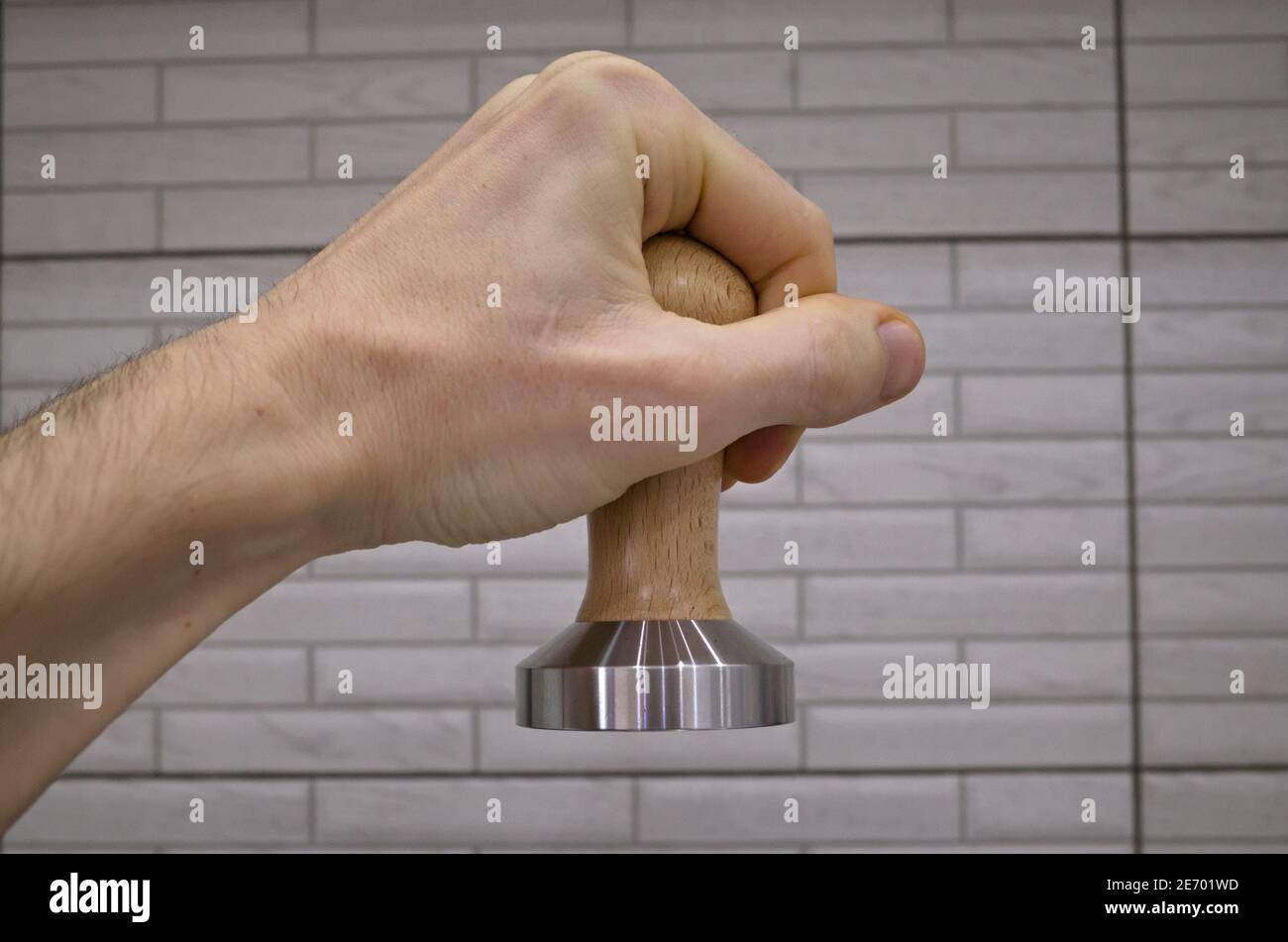 Manomissione a mano maschile per la pressione del caffè macinato per la preparazione di una bevanda espresso in una macchina da caffè. Apparecchiatura barista antimanomissione con manico in legno Foto Stock