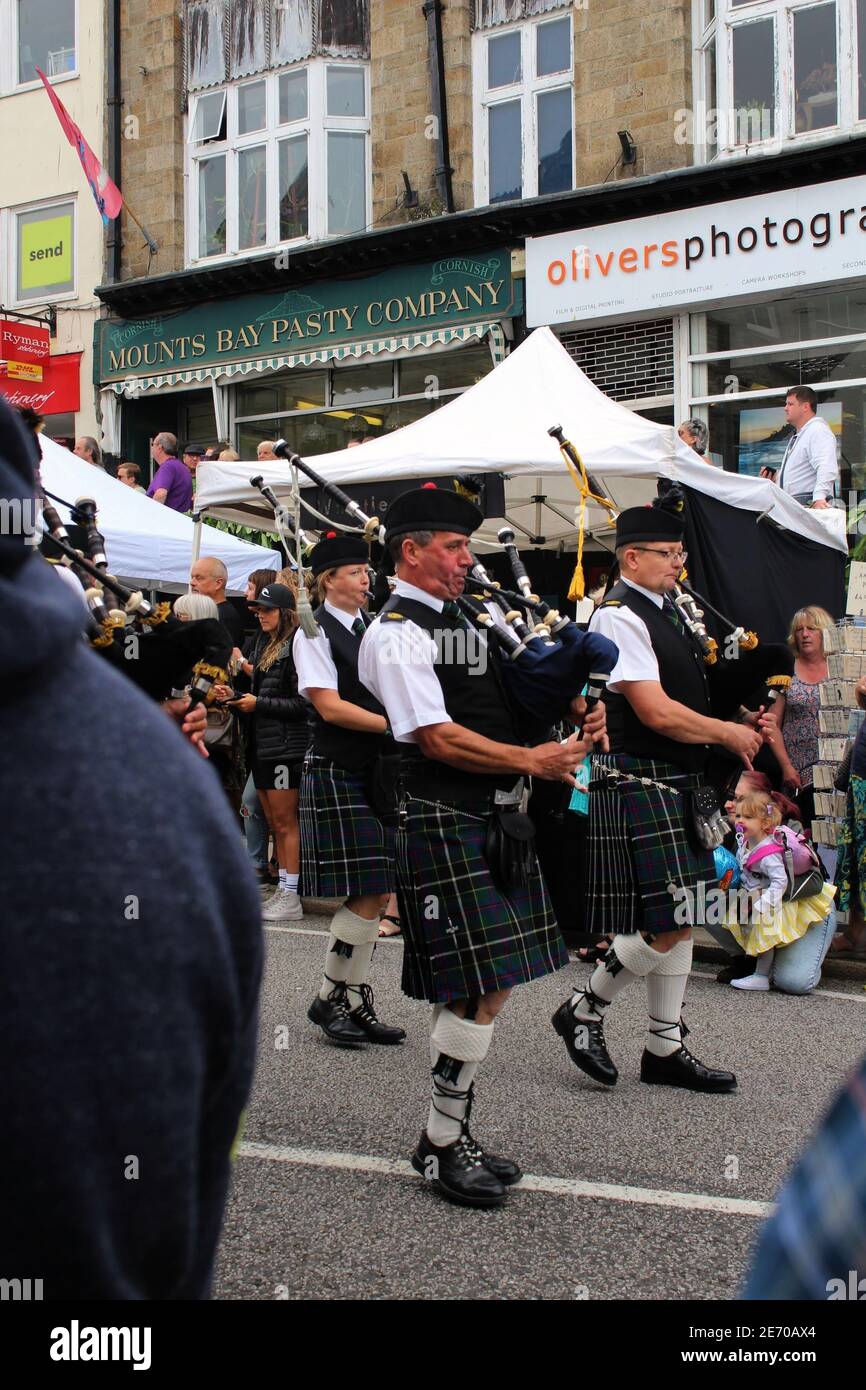 La gente che gioca le cornamuse e che indossa i kilt cammina attraverso Penzance As Parte della sfilata del Mazey Day 2019 per il festival di Golowan Foto Stock