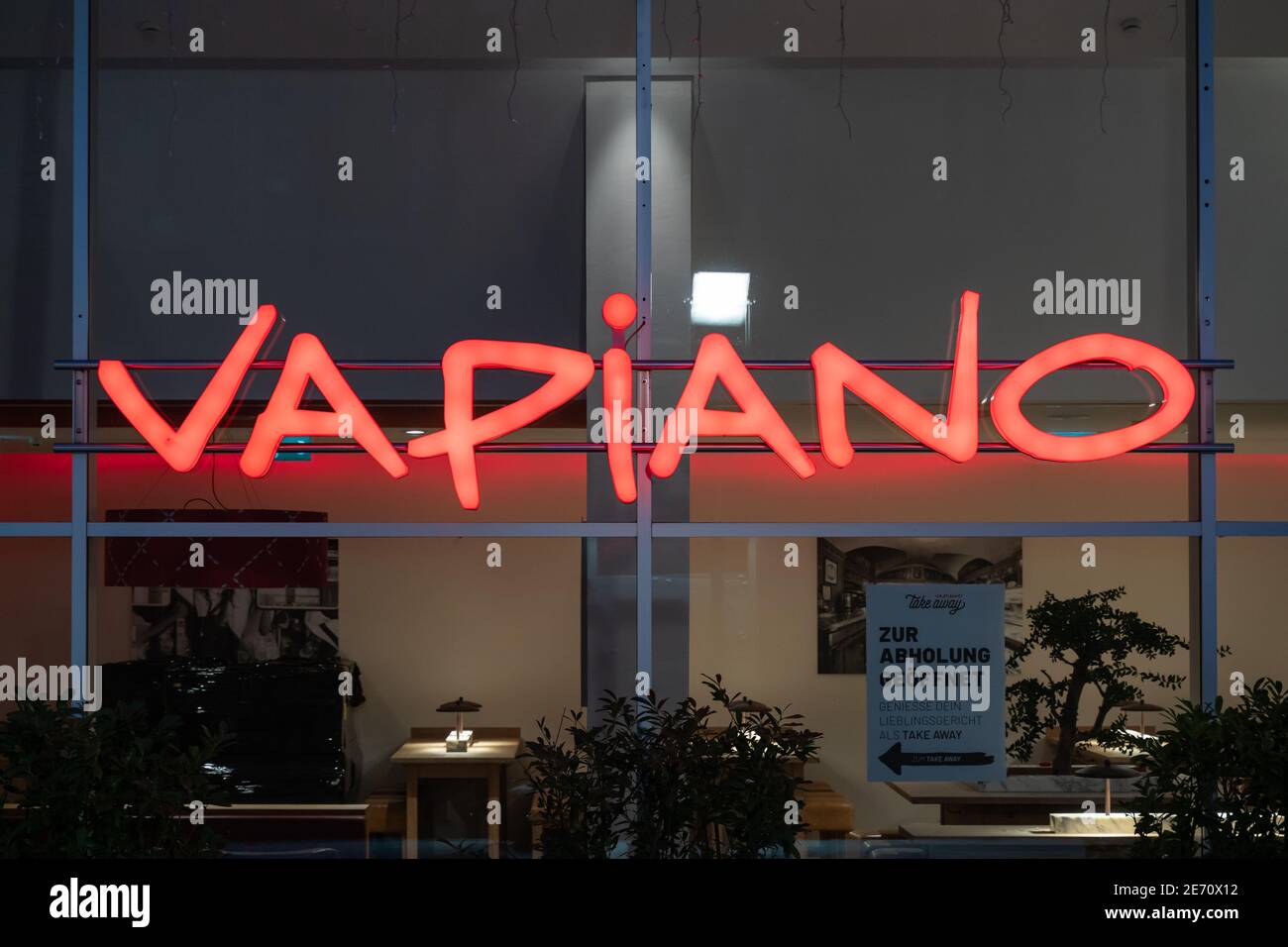 Logo Vapiano sulla parete illuminato in rosso. Catena di ristoranti in franchising che serve piatti italiani in Germania. Di fronte all'edificio in serata. Foto Stock
