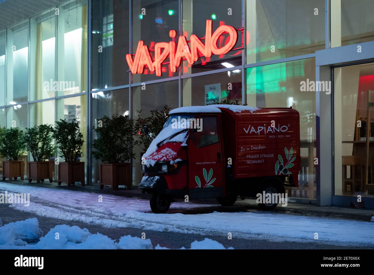 Logo Vapiano sulla parete illuminato in rosso. Catena di ristoranti in franchising che serve piatti italiani in Germania. Di fronte all'edificio in serata. Foto Stock