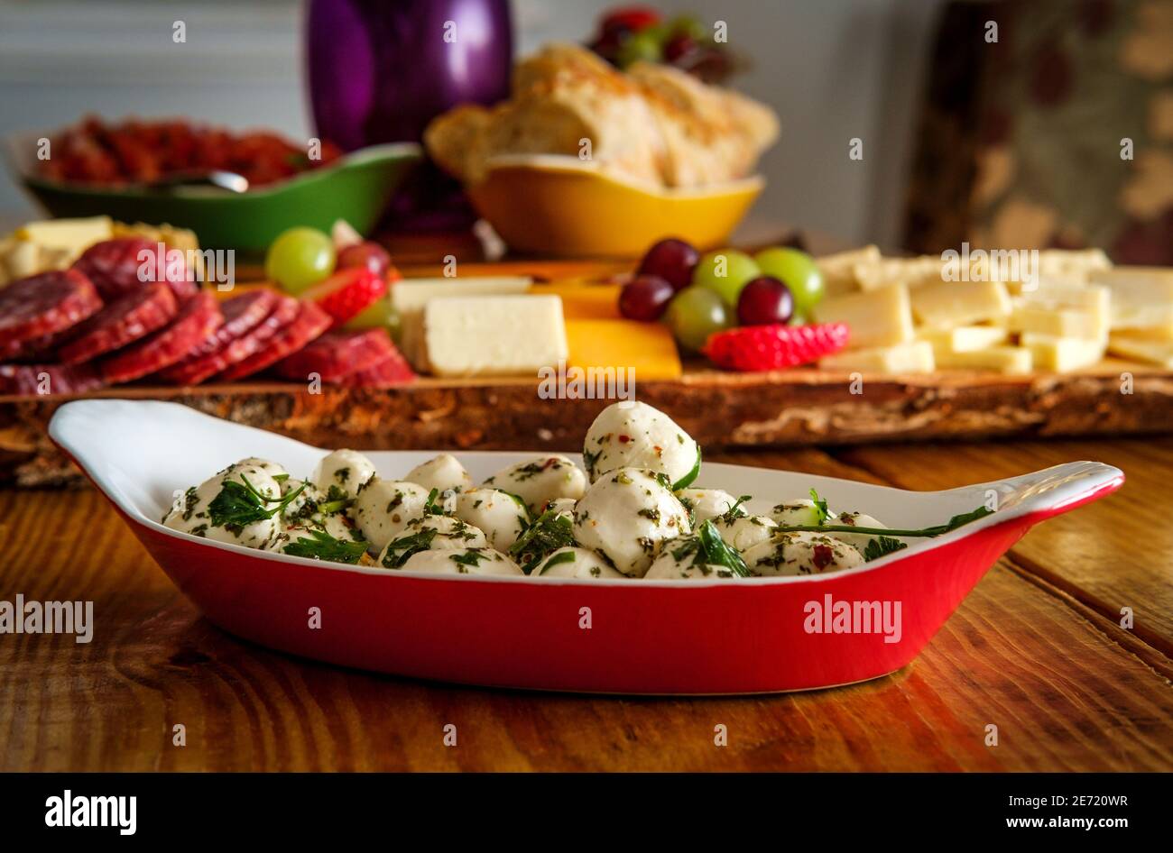 Insalata di mozzarella di bocconcini marinata con basilico servita in ovale teglia in porcellana di lasagne con salumi e piatto di formaggi nel backgro Foto Stock