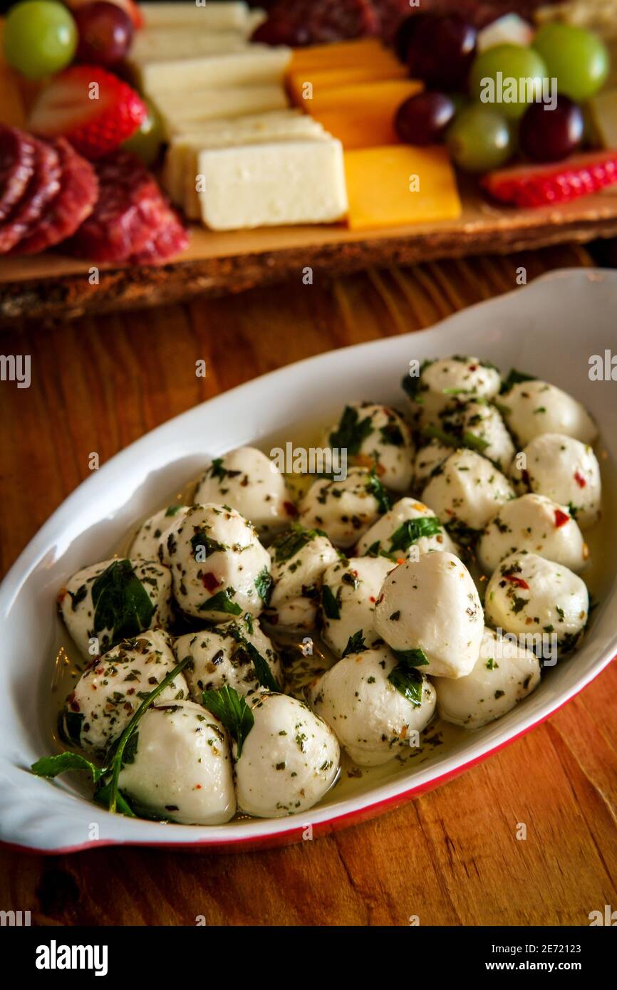Insalata di mozzarella di bocconcini marinata con basilico servita in ovale teglia in porcellana di lasagne con salumi e piatto di formaggi nel backgro Foto Stock