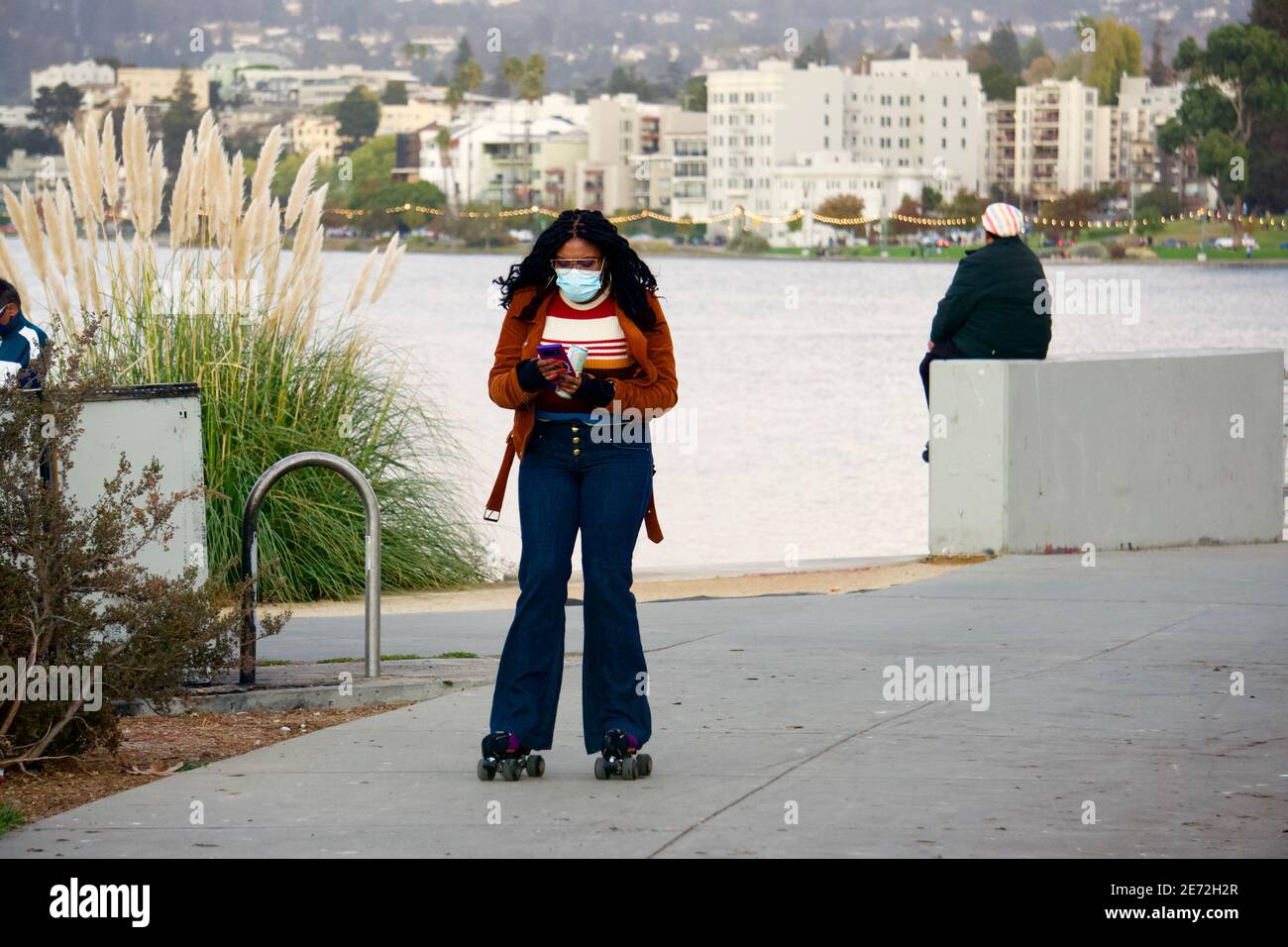 Donna su pattini a rotelle che guardano il suo telefono delle cellule al lago Merritt che dirige verso un raduno esterno del pattino a rotelle. Oakland, California, Stati Uniti Foto Stock