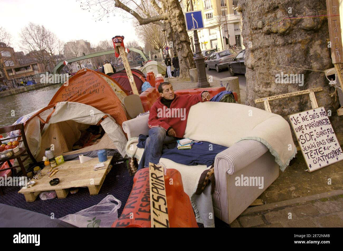 Una persona senza dimora non identificata si siede su un divano accanto  alle tende allestite lungo il Canal Saint Martin a Parigi, in Francia, il  19 febbraio 2007, come un piccolo gruppo