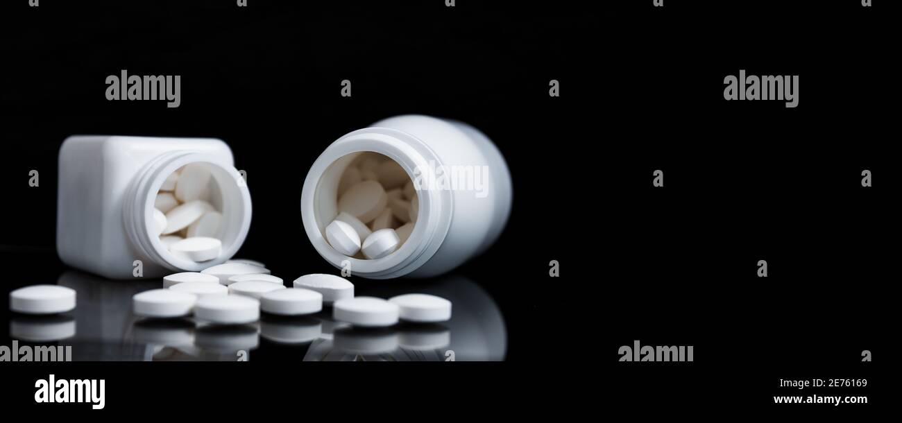 Pillole bianche e flaconi di medicina su sfondo nero. Foto Stock