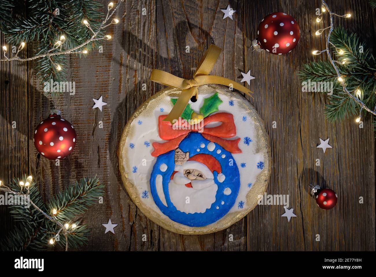 Pan di zenzero ornato decorato con Santa sorridente da Natale bauble. Piatto natalizio con ramoscelli in abete, baubles rossi e luci natalizie. Legno scuro Foto Stock