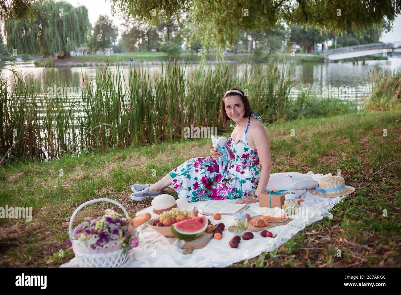 Una giovane donna si siede su un picnic in un parco sulle rive di un fiume Foto Stock