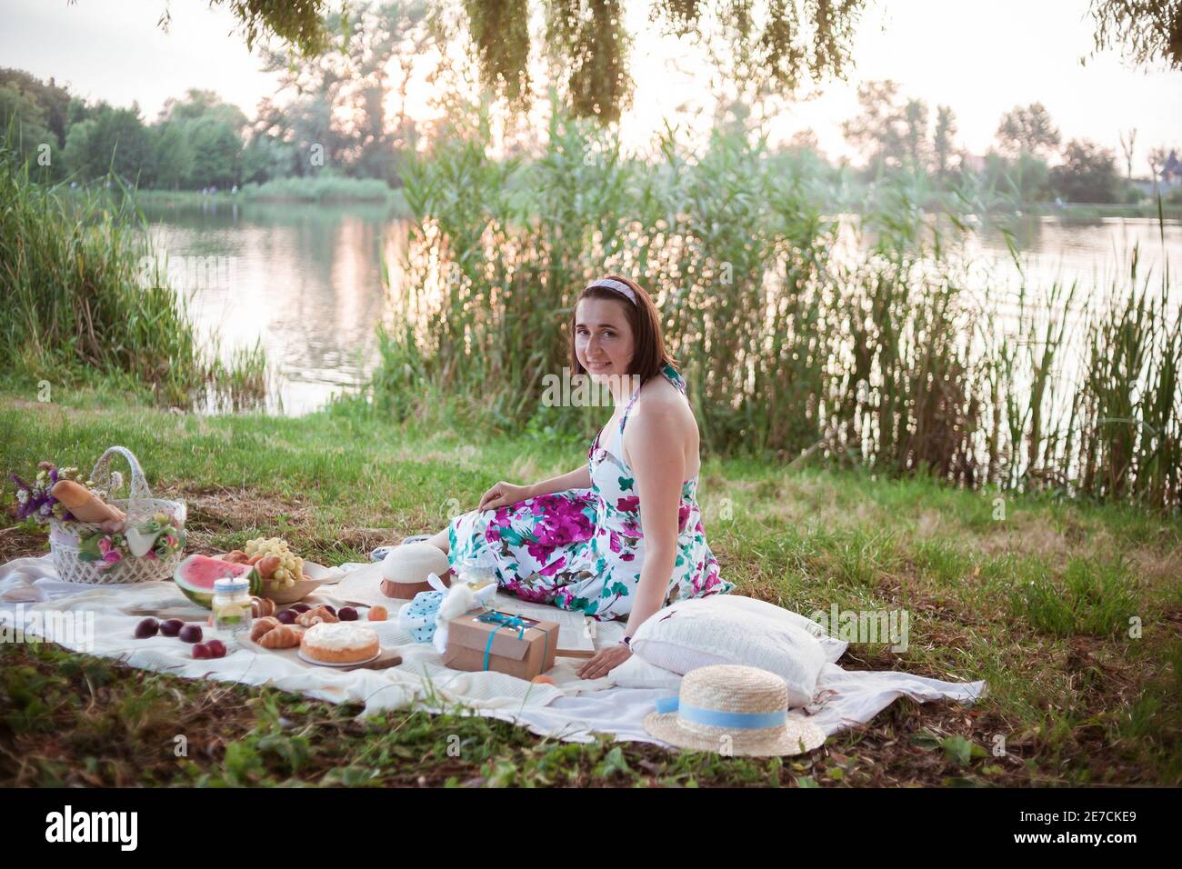 Una giovane donna si siede su un picnic in un parco sulle rive di un fiume Foto Stock