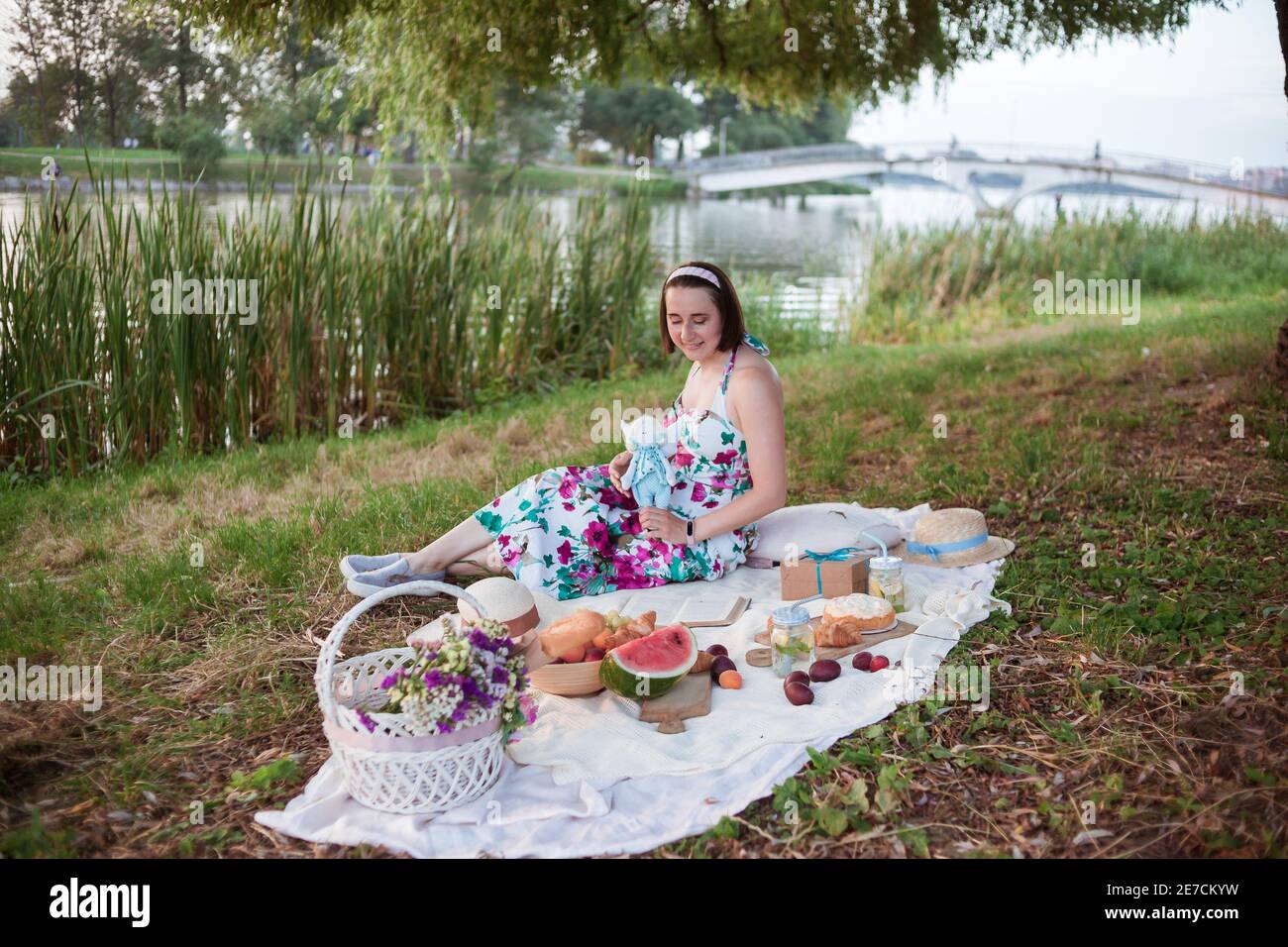Una giovane donna si siede su un picnic in un parco sulle rive di un fiume Foto Stock