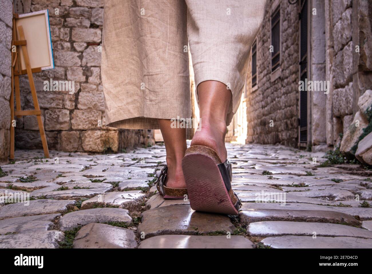 Foto dettagliata delle gambe femminili indossando comodi sandali da viaggio a piedi su vecchie strade di ciottoli medievali che drappeggiano il tour panoramico della città. Viaggi, turismo Foto Stock