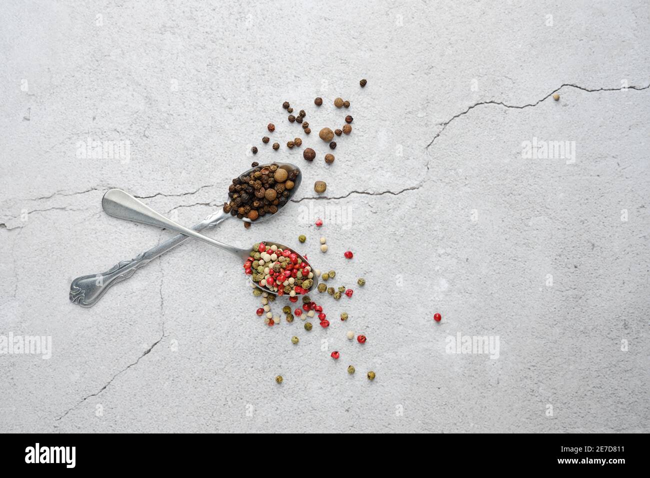 Due cucchiai incrociati con diversi tipi di pepe su cemento sfondo Foto Stock