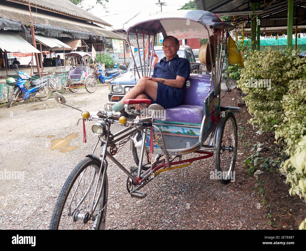 Un vecchio pedicab autista, sorridente in posa mentre attende i passeggeri in arrivo Foto Stock
