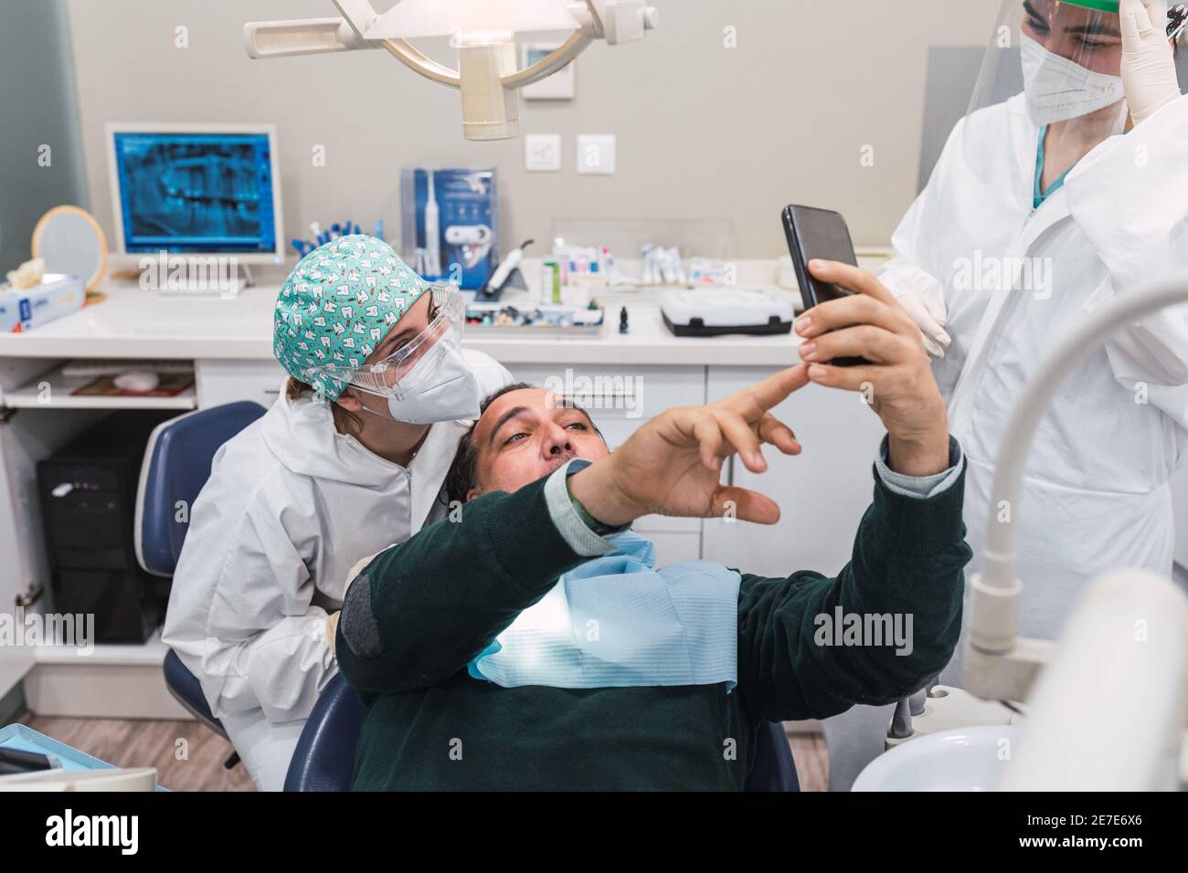 Paziente che prende un selfie nello studio dentistico. Tre persone. Medico femminile. Concetto di accoglienza e benessere. Sorrisi Foto Stock