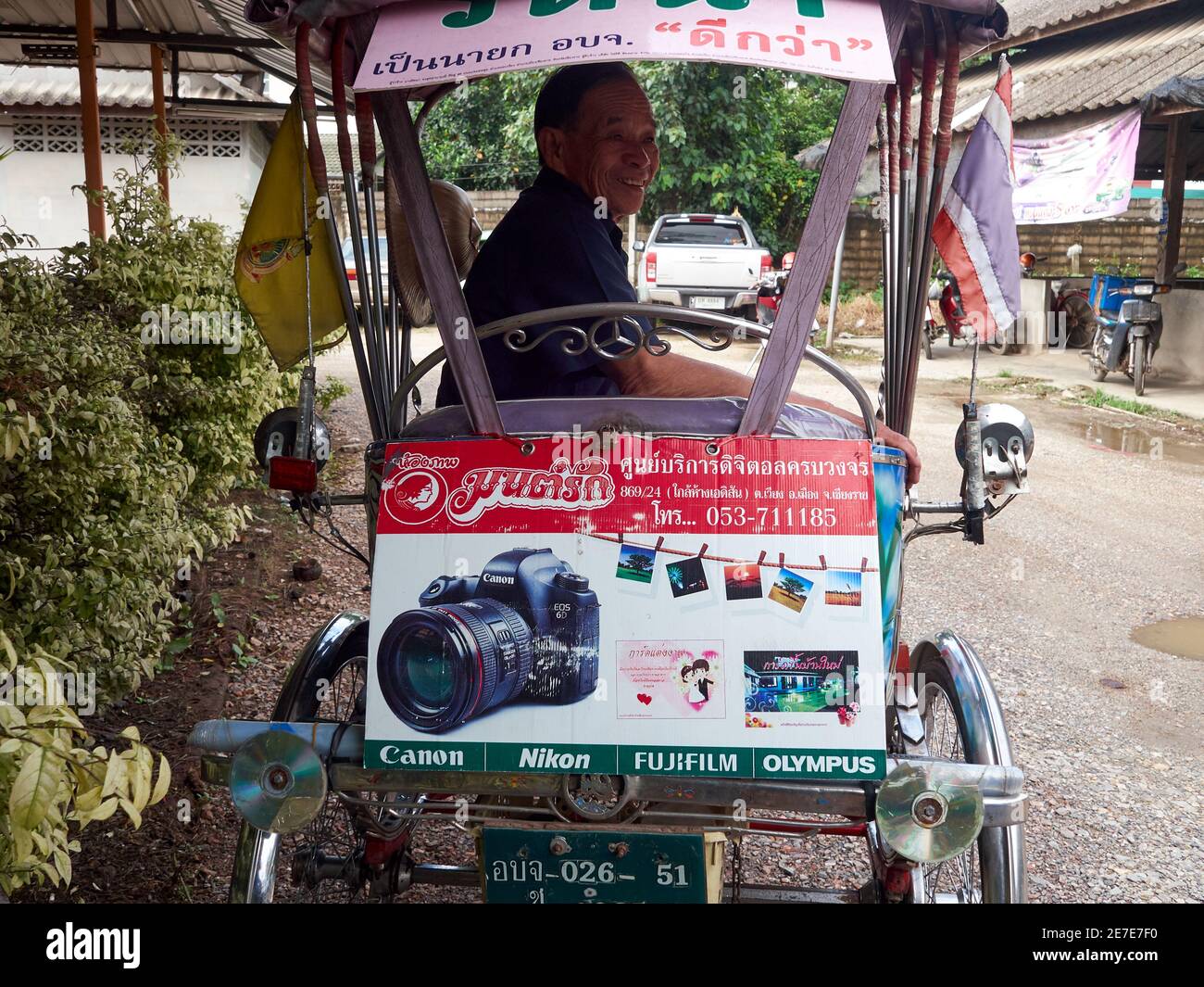 Un vecchio, un driver pedicab, sorride nel suo risciò che è sponsorizzato da una macchina fotografica Foto Stock
