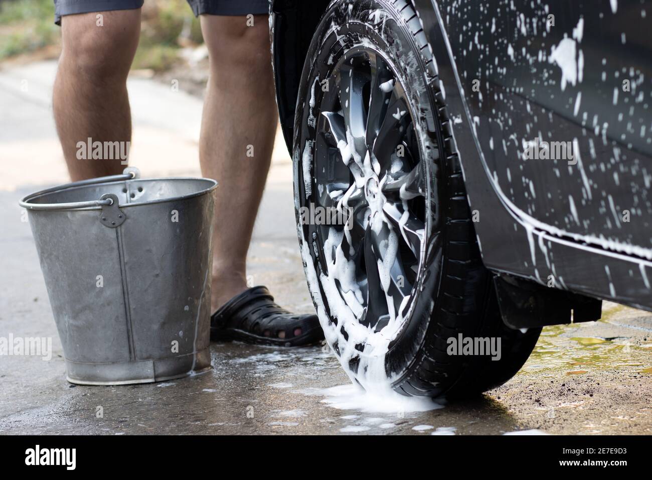 Un uomo con secchio che lava un'auto con acqua saponata. Foto Stock