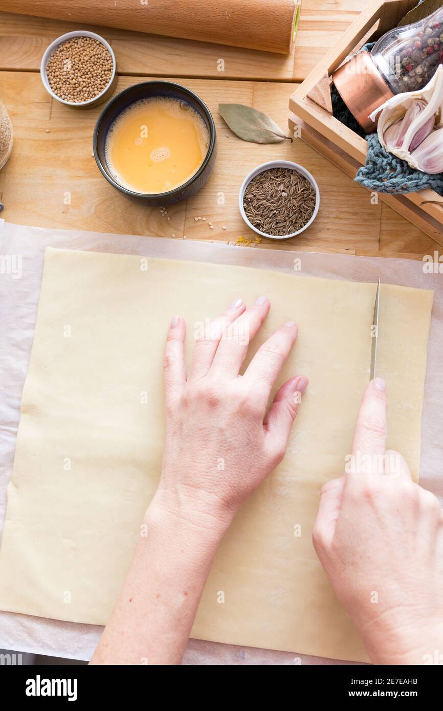 Le mani della donna tagliano una pasta sfoglia rettangolare. Foto Stock