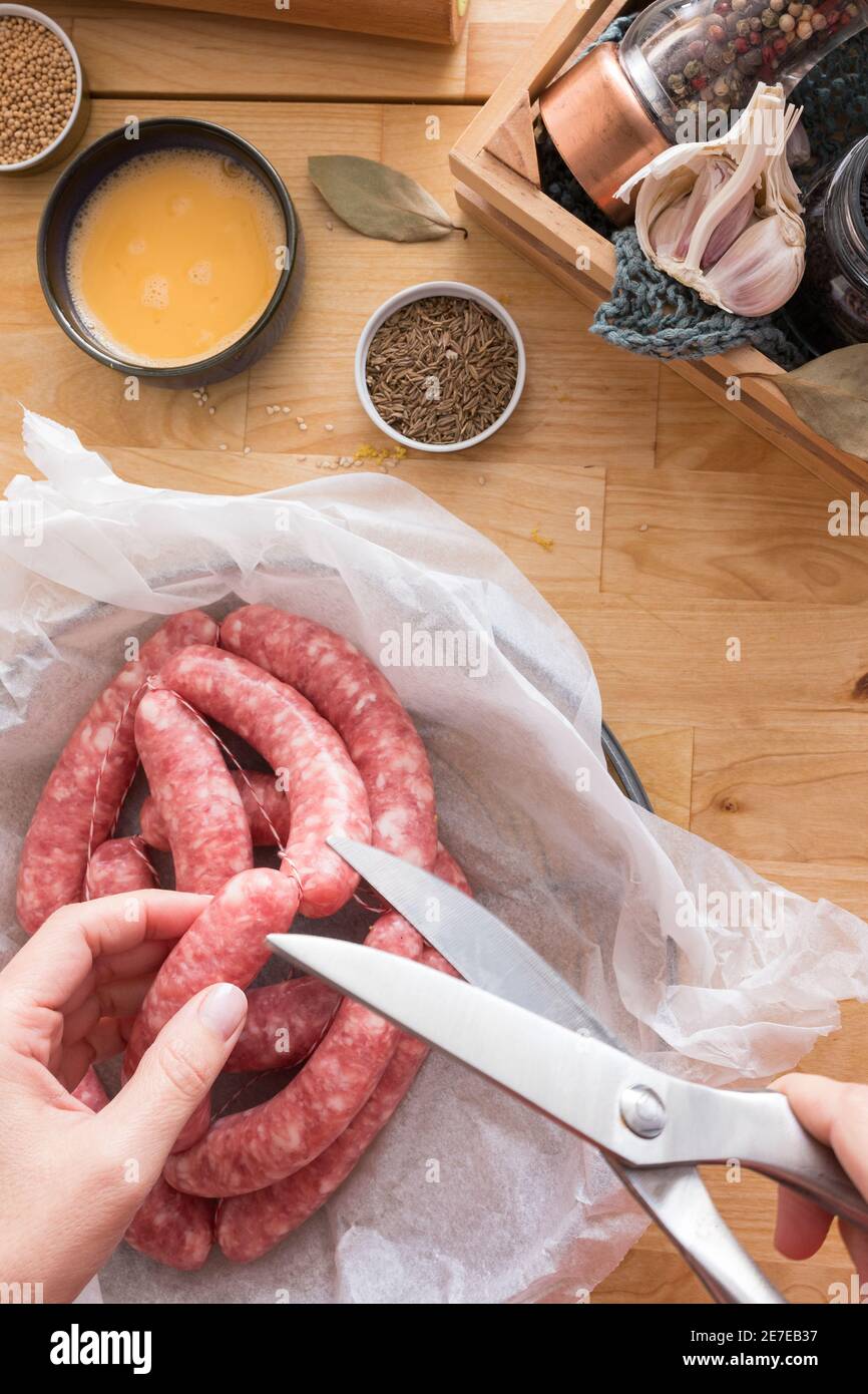 Vista closeup di una mano donna che taglia una corda di salsiccia con un paio di forbici. Foto Stock