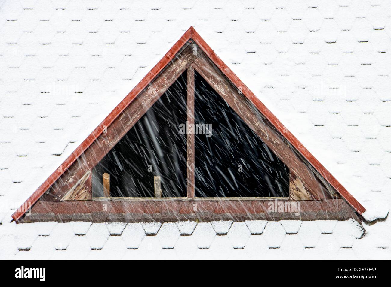 Il dormitorio senza vetro nelle finestre sul tetto nevoso. Caduta di neve sul tetto della casa con una finestra senza vetro. Foto Stock