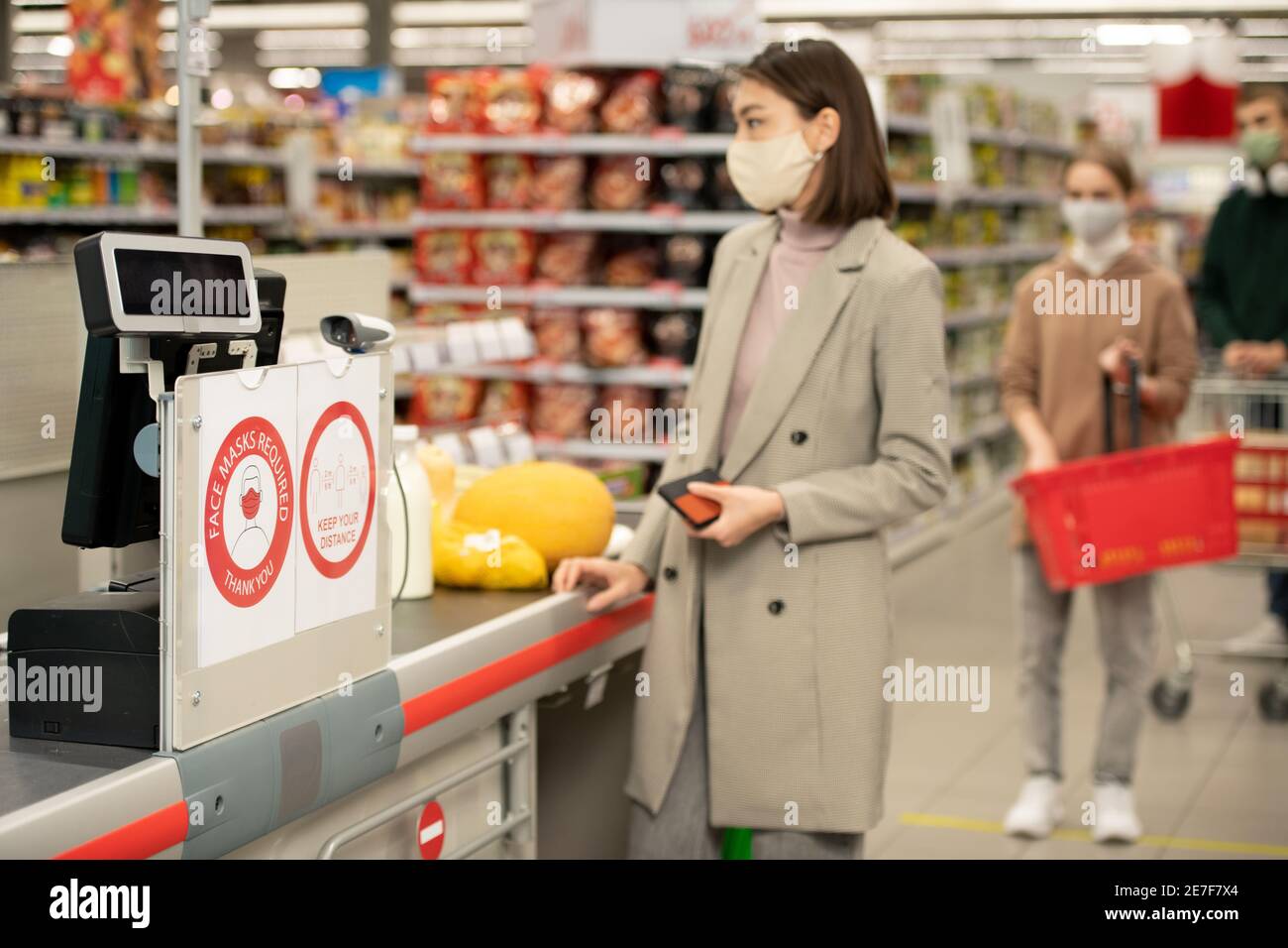 Cartone di plastica sul banco di cassa nel moderno supermercato annunciando il requisito su indossare maschere di protezione durante il periodo epidemico Foto Stock