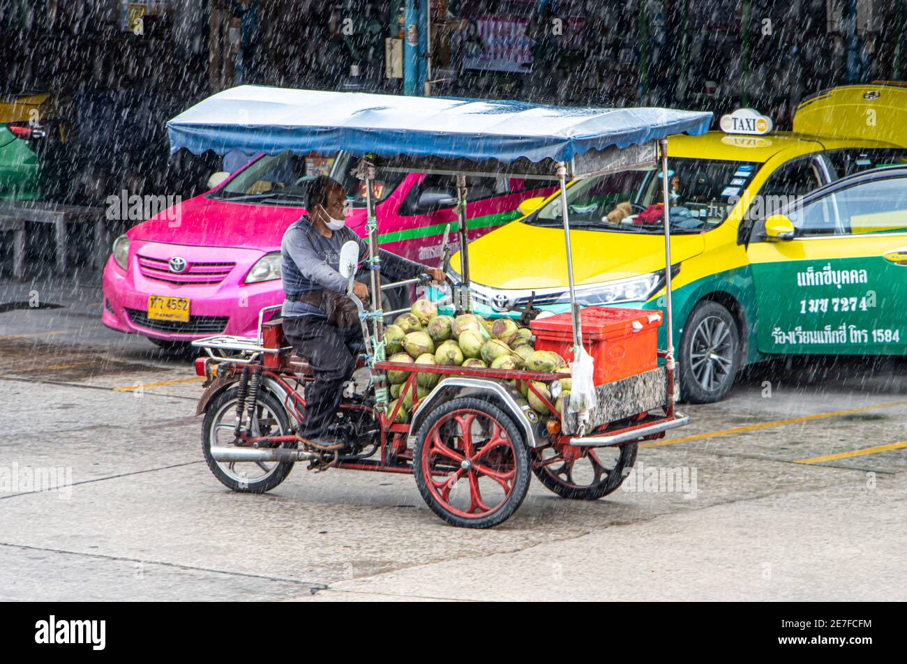 SAMUT PRAKAN, THAILANDIA, 21 2020 LUGLIO, il venditore di frutta guida una moto a tre ruote sotto la pioggia Foto Stock
