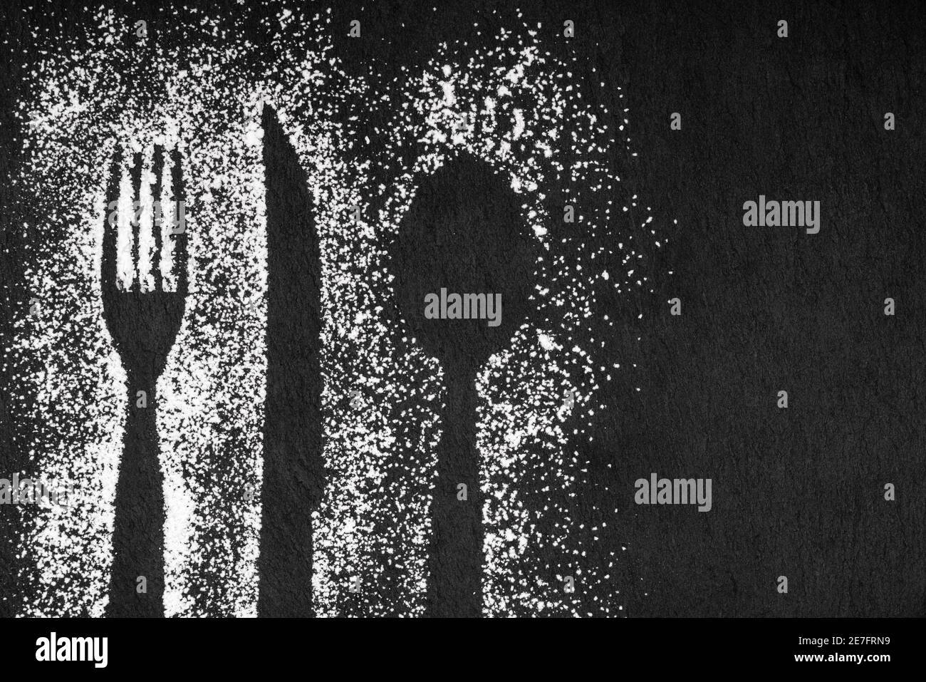 Sfondo di ardesia nera con cucchiaio e forchetta impresso su farina e coltello, immagine concettuale. Spazio di copia Foto Stock