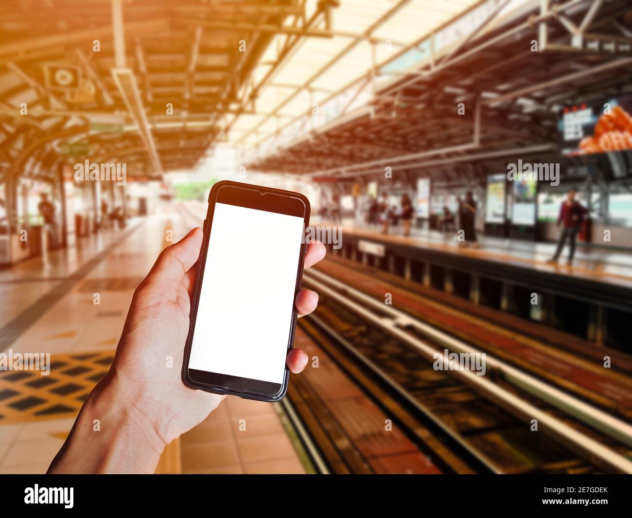 Smartphone nero con tenuta a mano e schermo vuoto davanti ai passeggeri in attesa del treno sulla piattaforma della stazione ferroviaria. Spazio per testo o des Foto Stock