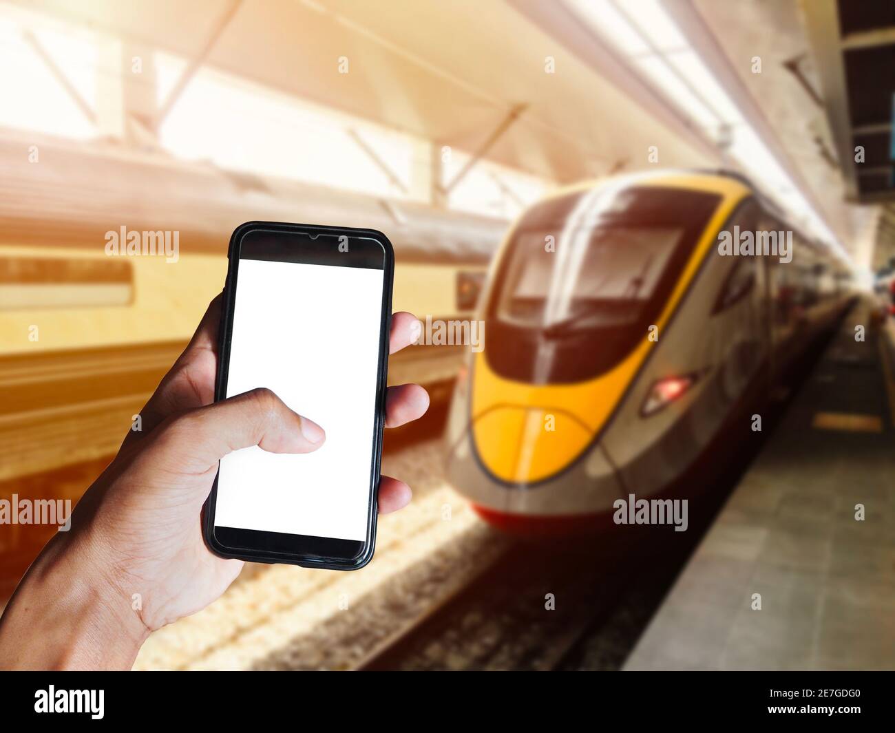 Uomo che tiene a mano smartphone nero con schermo vuoto di fronte al moderno treno che si dirige alla stazione ferroviaria. Spazio per testo o disegno Foto Stock